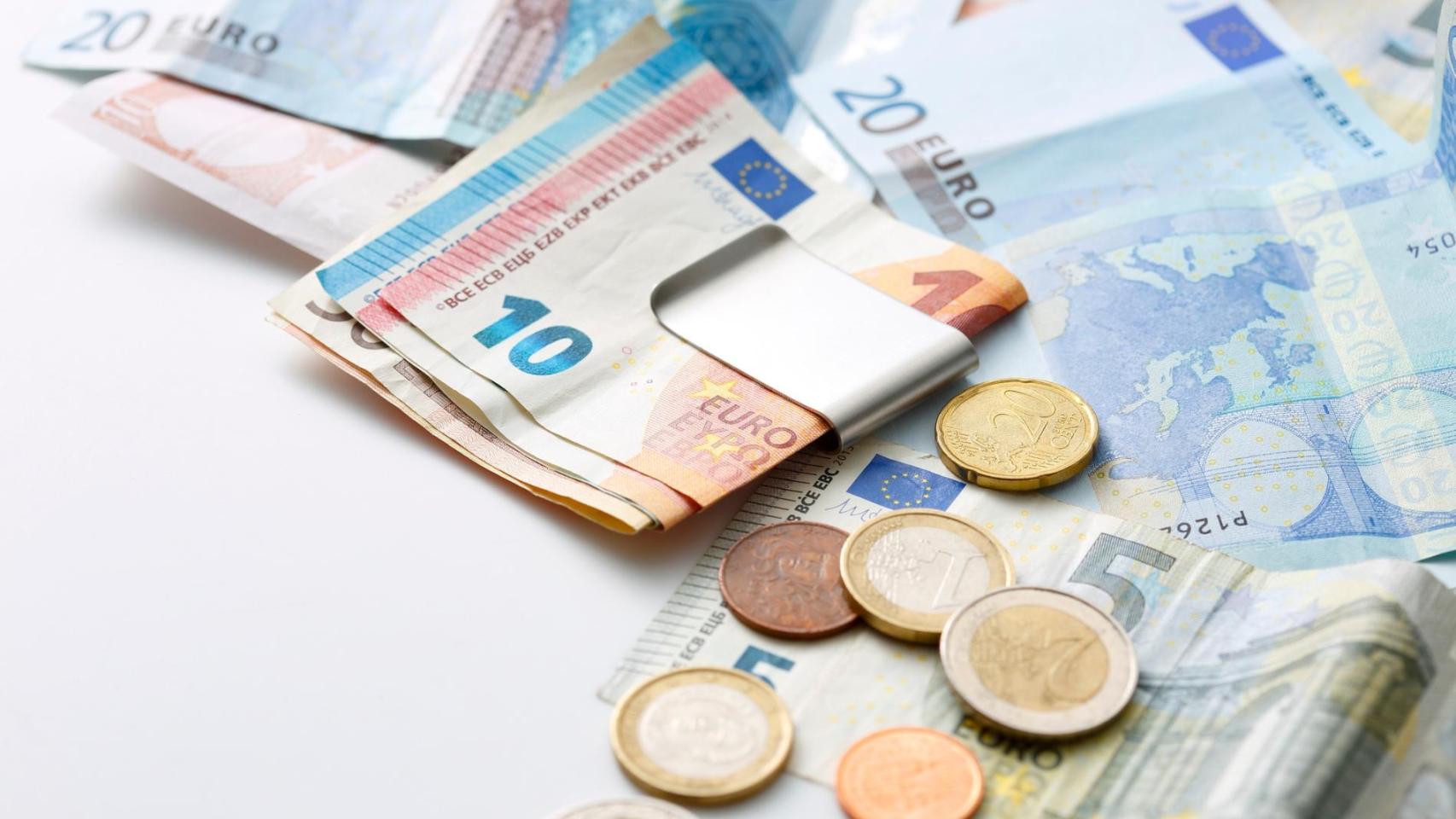 Billetes y monedas de euro sobre una mesa, imagen relacionada con el dinero en efectivo que debes guardar en casa para emergencias.