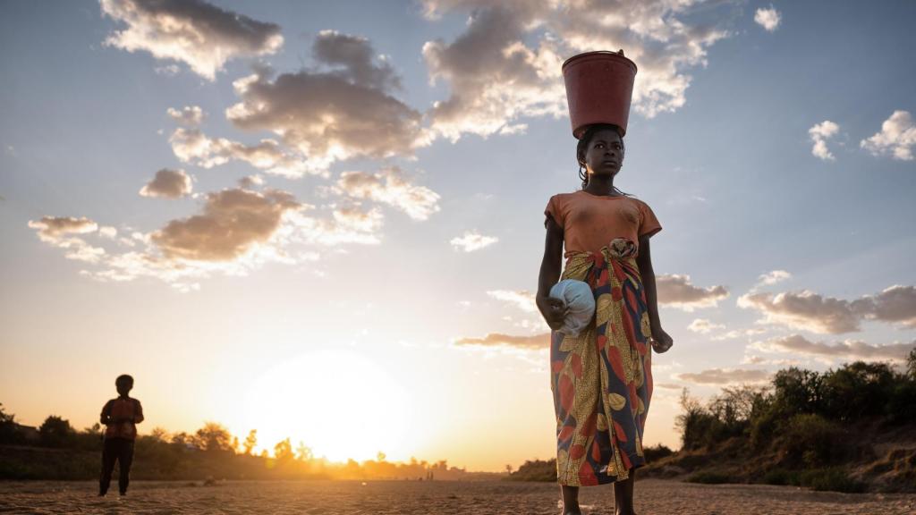 Una mujer de pie en el lecho seco del río Menarandra (Madagascar), cargando un cubo rojo lleno de agua sobre la cabeza mientras regresa a casa
