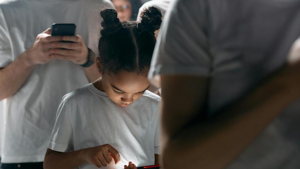 Una niña menor de edad utiliza su teléfono inteligente entre la multitud de gente