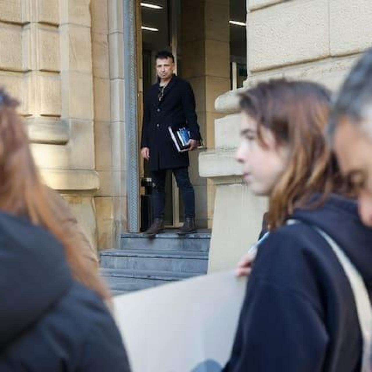 El acusado, Jon Perurena, observa una concentración en su contra en la Audiencia de Gipuzkoa, antes de arrancar el juicio contra este profesor para el que la Fiscalía solicita penas que suman 22 años de cárcel, acusado de solicitar favores sexuales a tres alumnas menores de edad de un centro educativo de Irun