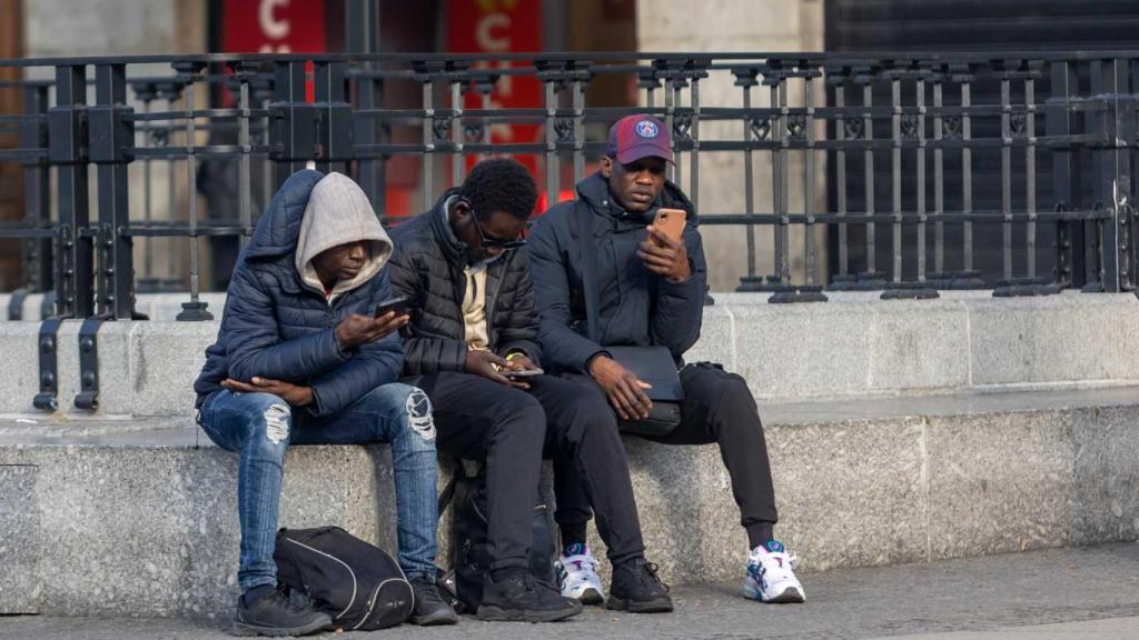 Tres personas miran el móvil. 