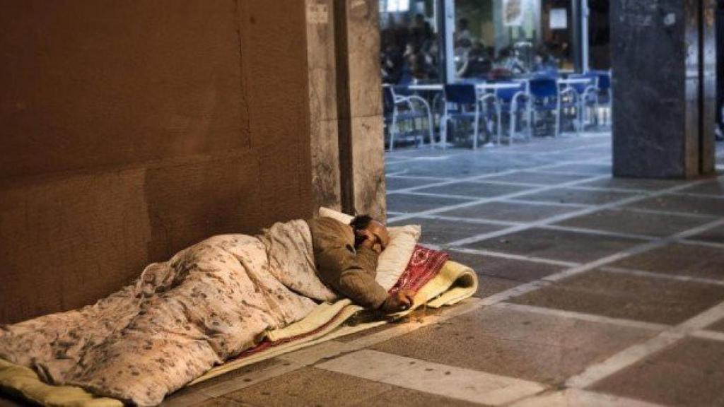 Un home sense sostre dorm a la vorera, al costat d'una cafeteria / EFE