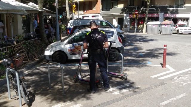 Un guardia urbano sanciona a dos patinetes eléctricos de una empresa estacionados en unos aparcamientos de bici / JORDI SUBIRANA