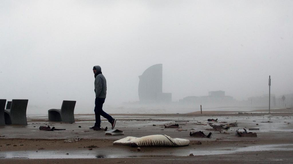Una persona pasea por la playa con el viento de cara durante el temporal Gloria que ha azotado Barcelona