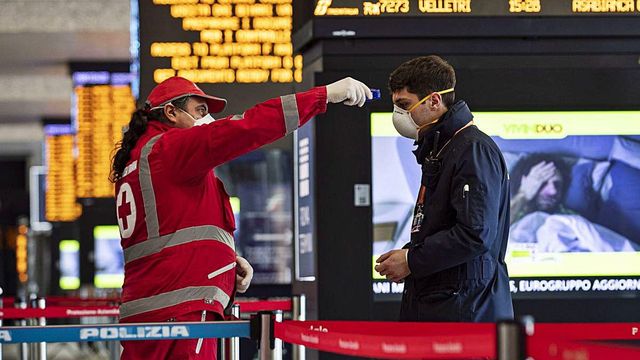 Un profesional tomando la temperatura a un pasajero en una estación de tren