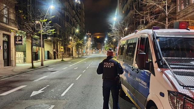 Un agente de la Guardia Urbana observa una calle vacía al lado de un furgón policial / AYUNTAMIENTO