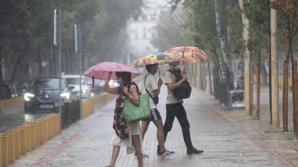 Una mujer y dos jóvenes pasean bajo la lluvia con paraguas