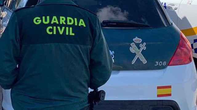 Un agente de la Guardia Civil de espaldas y junto a un vehículo oficial del cuerpo