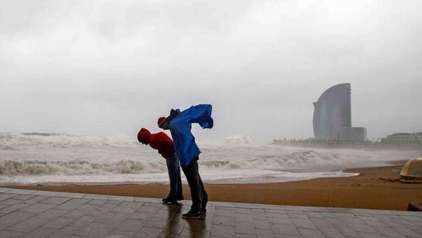 Dos personas intentan que no las tumbe el viento durante un fuerte temporal en Barcelona / EFE