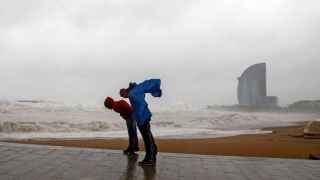 Dos personas intentan que no las tumbe el viento durante un fuerte temporal en Barcelona / EFE