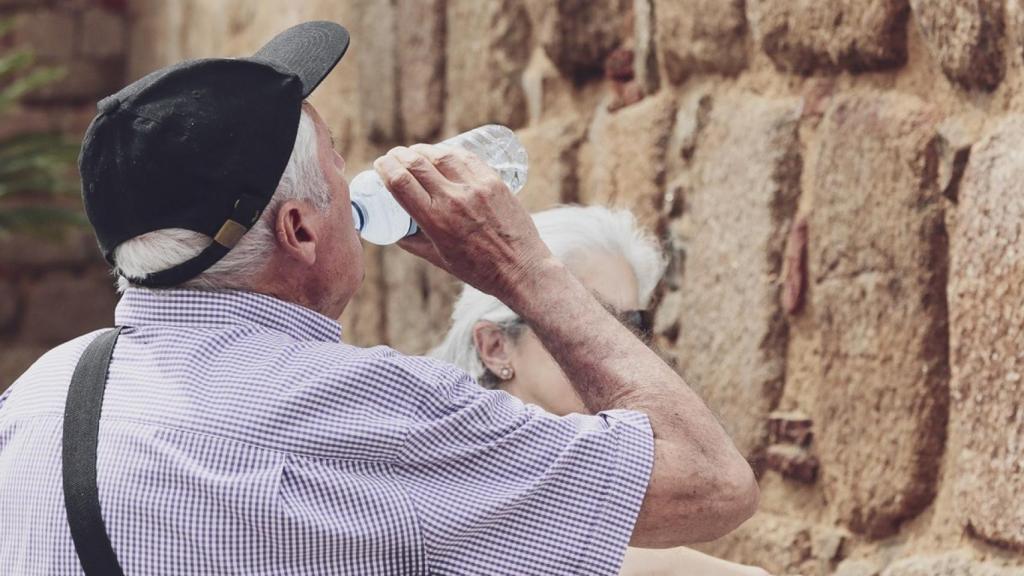 Un hombre mayor bebe agua de una botella en un día de intenso calor