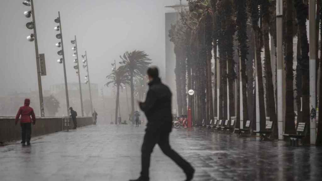 Un home camina sota la pluja pel passeig marítim de Barcelona