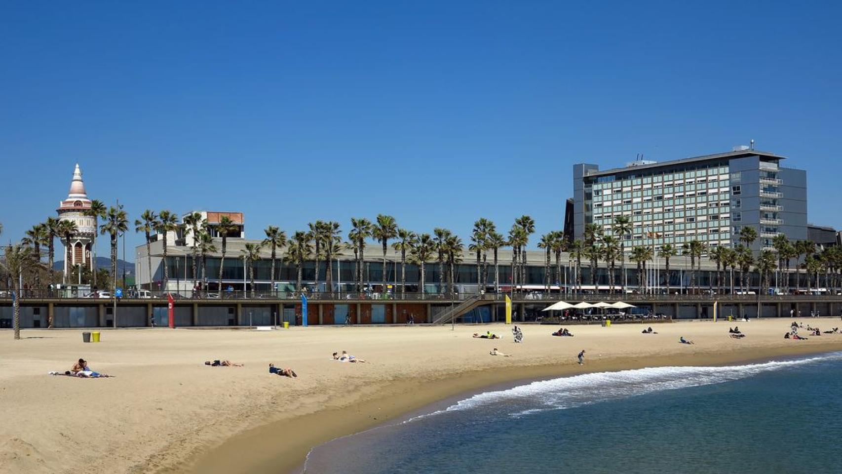 Playa del Somorrostro, en la Barceloneta, Barcelona, con varias personas tomando el sol frente al Hospital del Mar