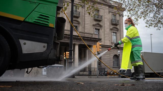 Una trabajadora riega una calle con una manguera en enero en Barcelona