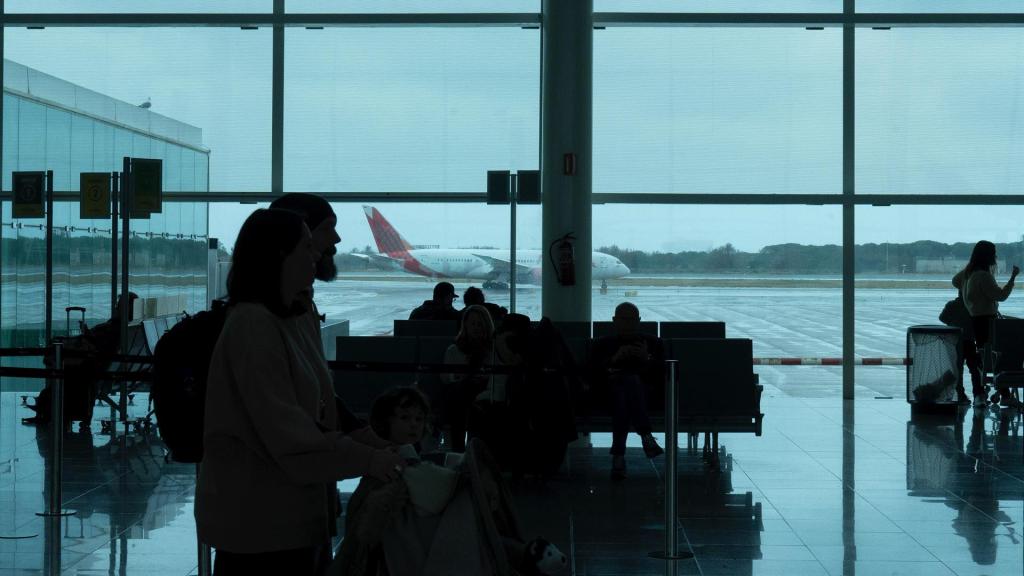 Varias personas esperan sentadas frente a un avión aparcado en la pista del aeropuerto de El Prat