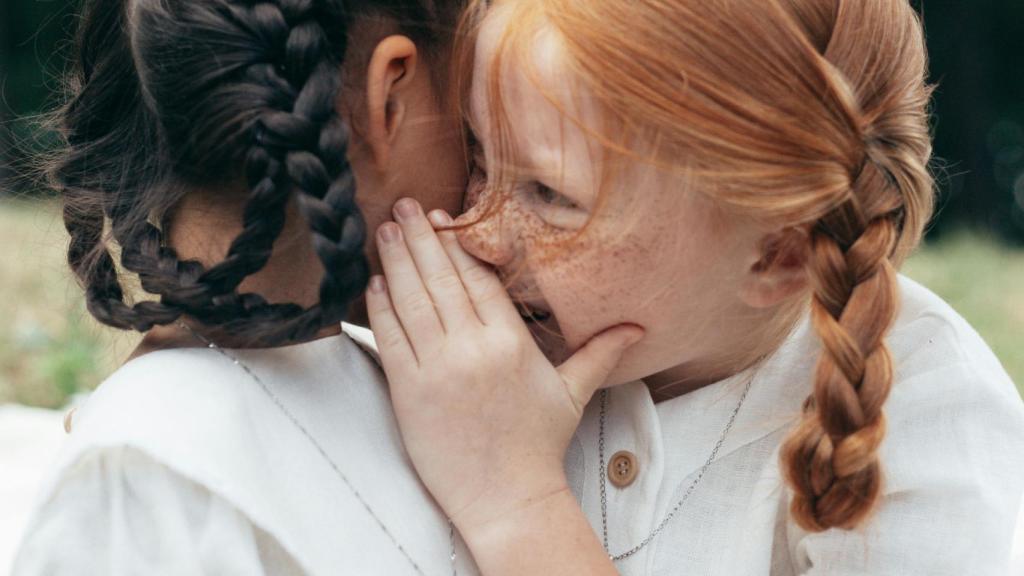 Una niña le susurra algo a otra a la oreja