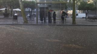 Varias personas esperan en la parada del bus durante la tormenta en Barcelona