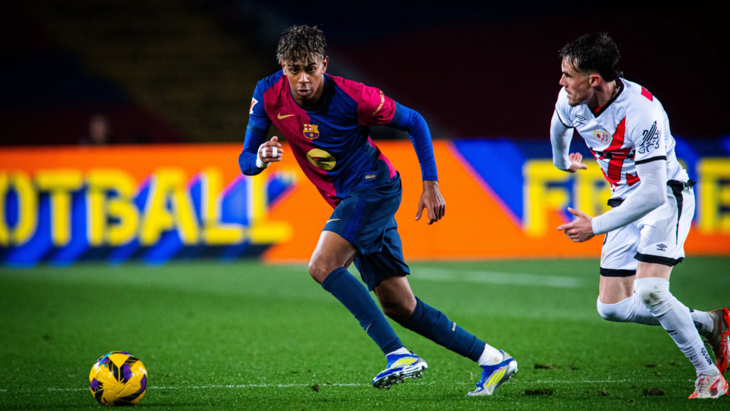 Lamine Yamal levanta la cabeza mientras conduce el balón frente a un jugador del Rayo Vallecano
