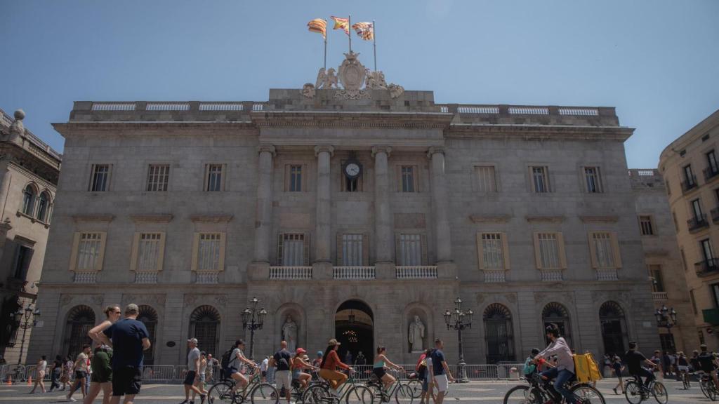 Varias personas caminan delante del edificio del Ayuntamiento de Barcelona.