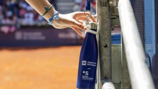 Cantimplora de Aigües de Barcelona con un campo de tenis de fondo