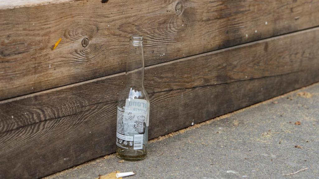 Una botella de cerveza vacía en los bancos frente a la Escola Aldana de Sant Antoni