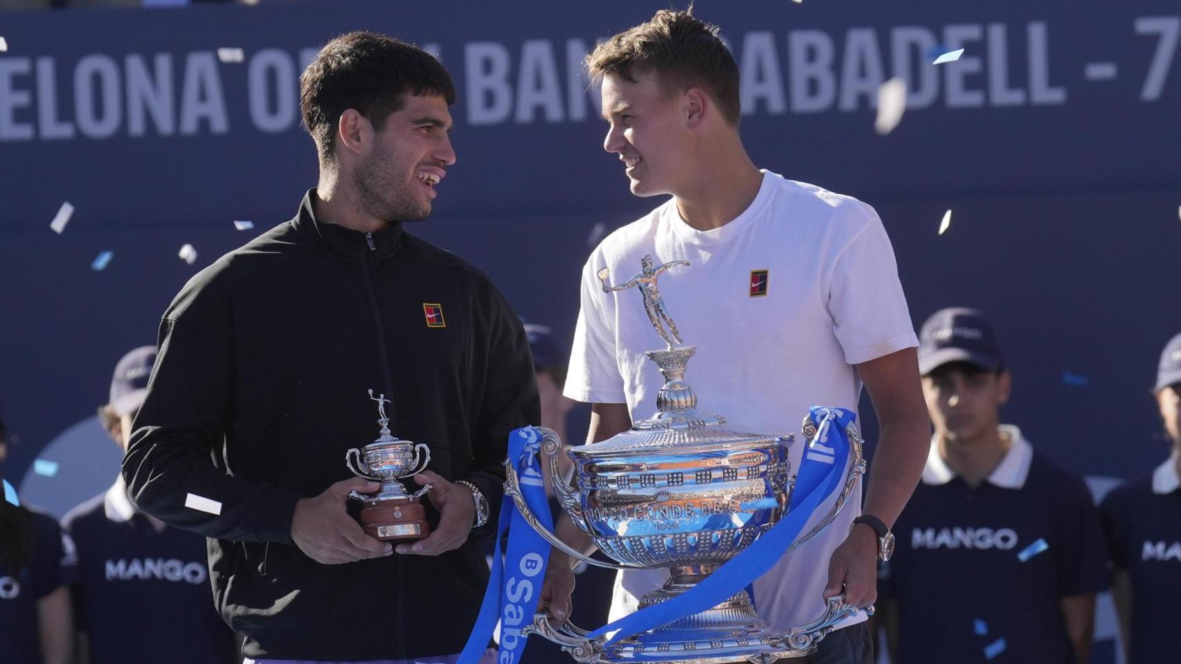 El tenista danés Holger Rune (d) con el trofeo tras su victoria ante el español Carlos Alcaraz (i) en la final del Barcelona Open Banc Sabadell-Trofeo Conde de Godó disputado este domingo en Barcelona