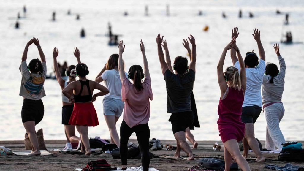 Expats practicant ioga a la platja de la Barceloneta a l'albada