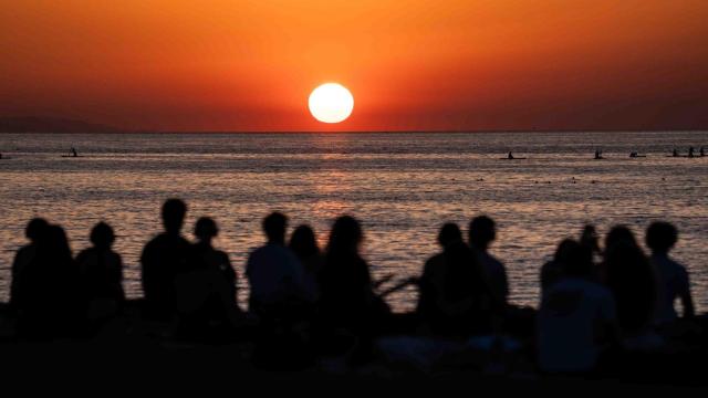Varias personas observan el amanecer desde la playa de Sant Sebastià de Barcelona en un evento de Showup