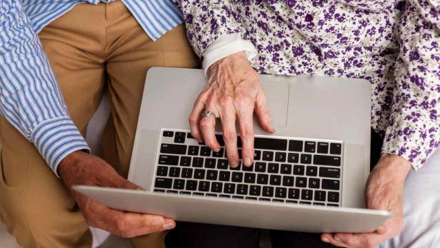 Persona mayor acompañada teclea en un portátil