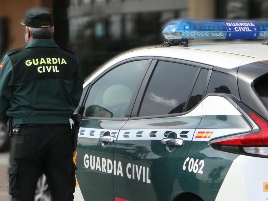 Un agent de la Guàrdia Civil, d'esquena, dret al costat d'un vehicle oficial.