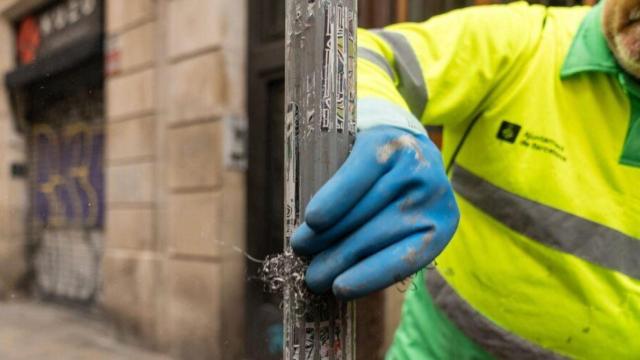 Un trabajador de limpieza del Ayuntamiento de Barcelona retira un cartel en la vía pública