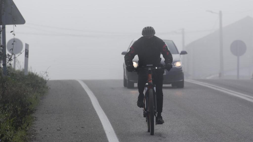 Un ciclista i un cotxe en una carretera amb boira.