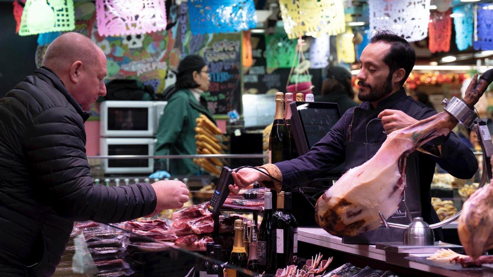 Un comerciante cobra a un cliente, en el Mercado de la Boquería, a 14 de diciembre de 2023, en Barcelona