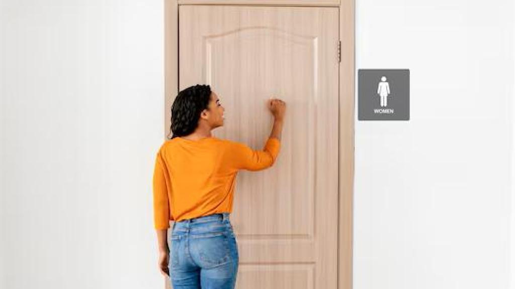 Persona tocando la puerta del lavabo