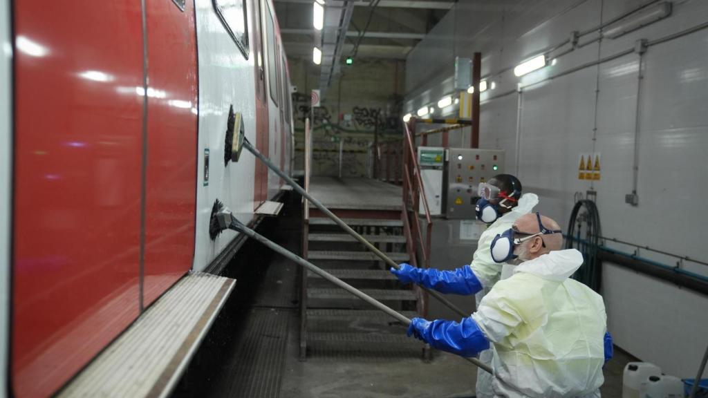 Dos empleados trabajan limpiando un tren durante una visita a los túneles de lavado y al espacio de limpieza de graffitis del metro de Barcelona