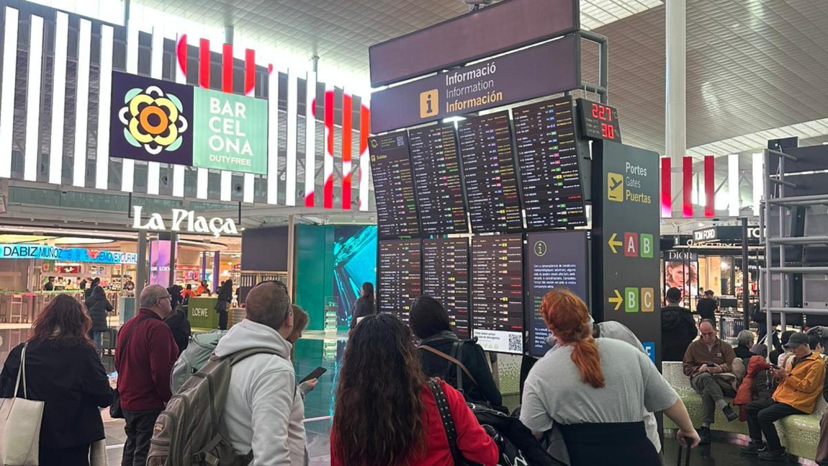 Viajeros observando las pantallas de información del Aeropuerto de Barcelona ante el temporal de viento