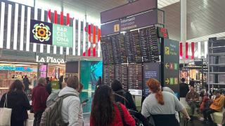 Viajeros observando las pantallas de información del Aeropuerto de Barcelona ante el temporal de viento