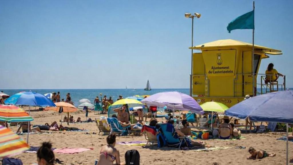 Bañistas junto a la torre de vigilancia de Pro-Activa en la playa de Castelldefels