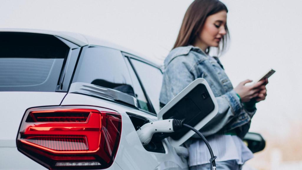 Mujer consulta su móvil mientras recarga su vehículo eléctrico